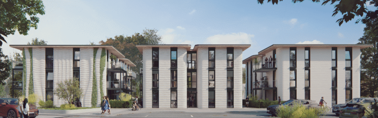 Moderne dreigeschossige Wohnanlage mit hellen Fassaden, großen Fenstern, Balkonen und begrünten Außenbereichen; davor eine Straße mit Autos und einer Person.
